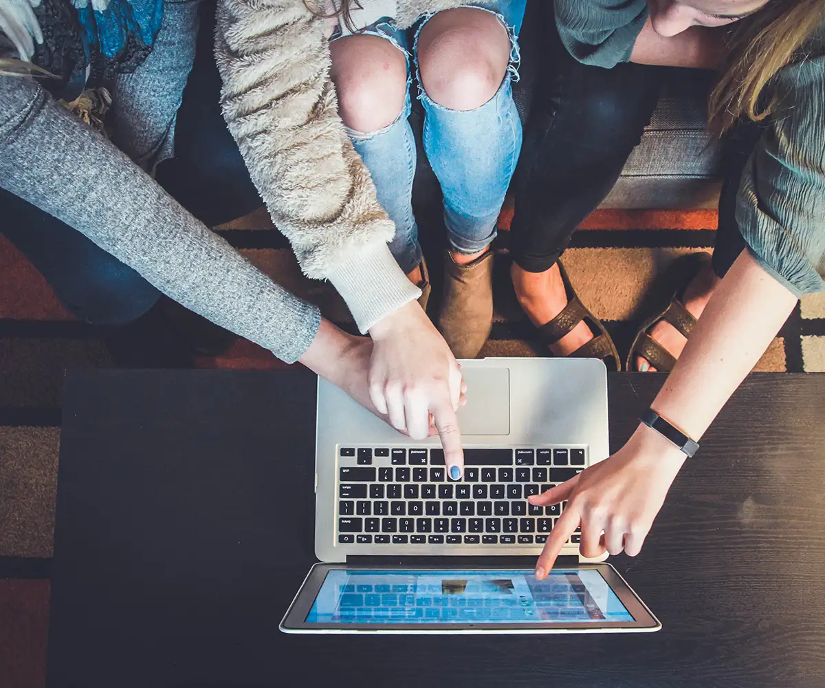 Drei Frauen sitzen auf einem Sofa und zeigen auf einen Laptop.