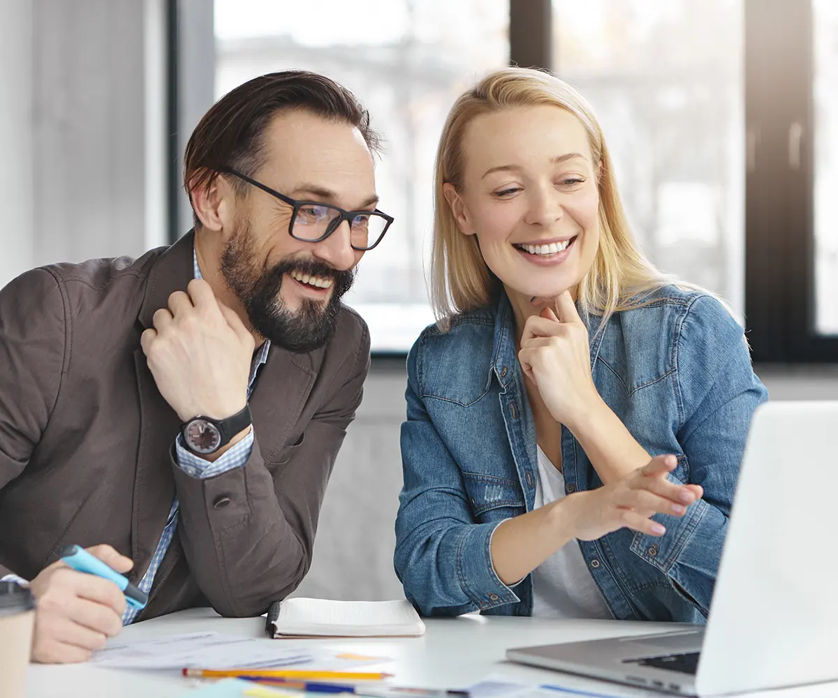 barrierefreiheitsgesetz - Vorteile für Unternehmen Ein Mann und eine Frau lächeln, während sie auf einen Laptop schauen